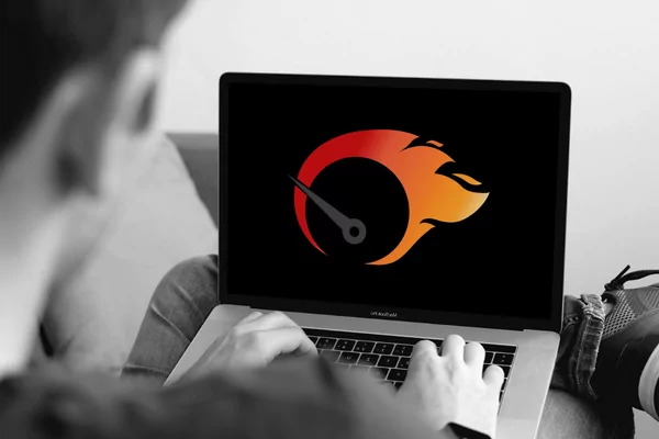 Schwarz-weisses Bild von einem Mann, der am Laptop sitzt. Auf dem Bildschirm ist ein flammender Tacho zu sehen in Rot-Orange.